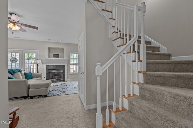 stairs with a tiled fireplace, carpet flooring, baseboards, and ceiling fan