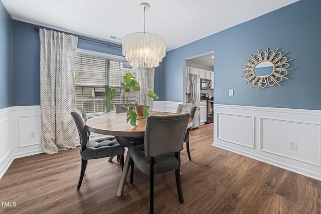 dining room featuring an inviting chandelier, visible vents, wainscoting, a decorative wall, and wood finished floors