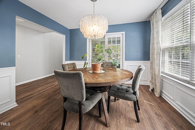 dining space featuring a chandelier, wainscoting, wood finished floors, and a decorative wall