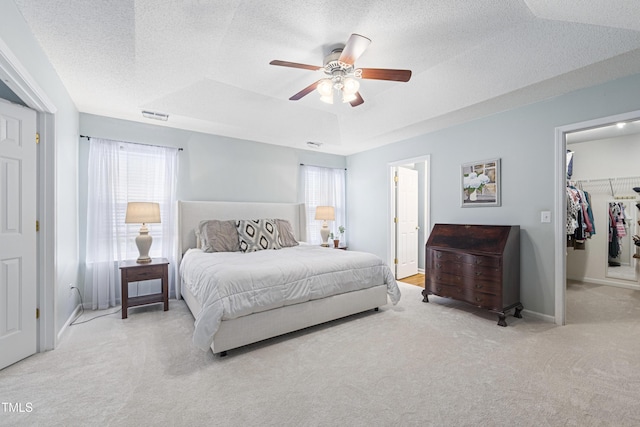 carpeted bedroom with a walk in closet, a ceiling fan, a textured ceiling, visible vents, and baseboards