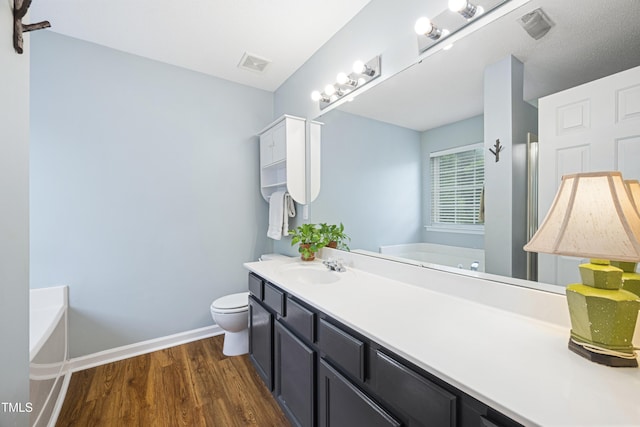 bathroom with vanity, toilet, wood finished floors, visible vents, and a garden tub