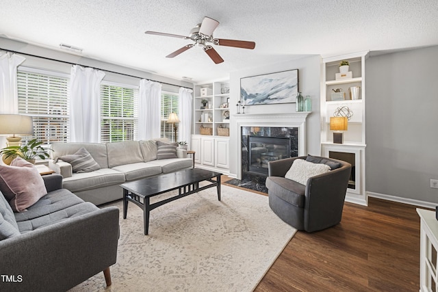 living area with ceiling fan, a fireplace, a textured ceiling, dark wood finished floors, and visible vents