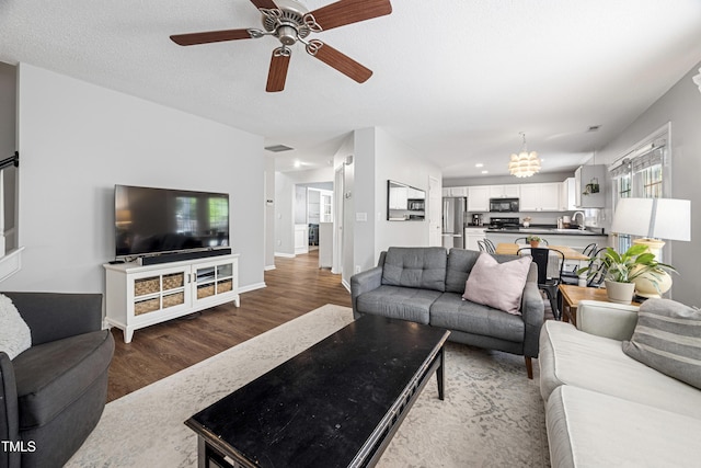 living area featuring baseboards, wood finished floors, and ceiling fan with notable chandelier
