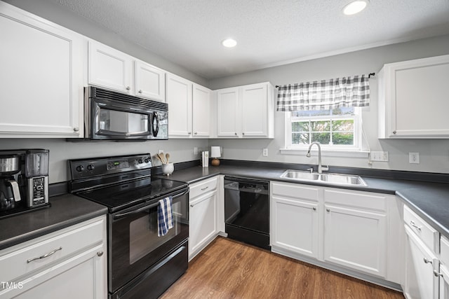 kitchen with white cabinetry, dark countertops, a sink, and black appliances