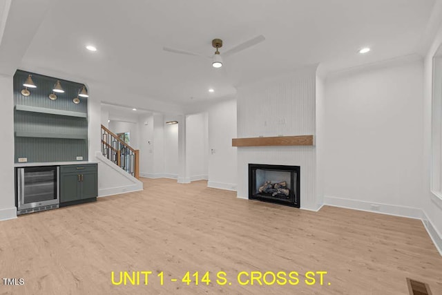 unfurnished living room featuring a fireplace, stairs, wood finished floors, beverage cooler, and recessed lighting