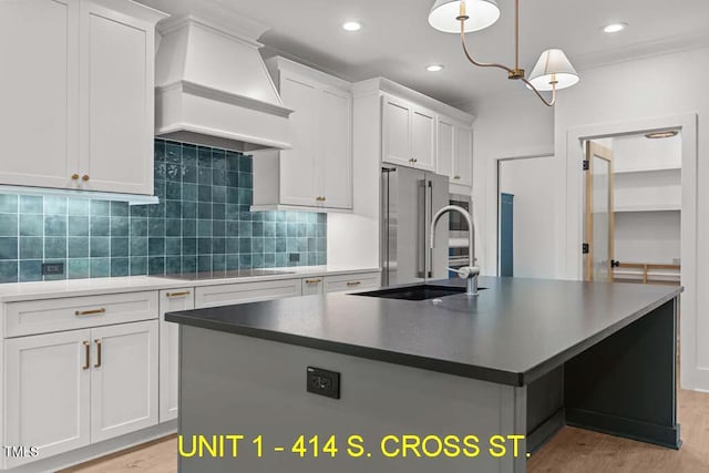 kitchen featuring light wood-type flooring, black electric cooktop, high end refrigerator, custom range hood, and an island with sink