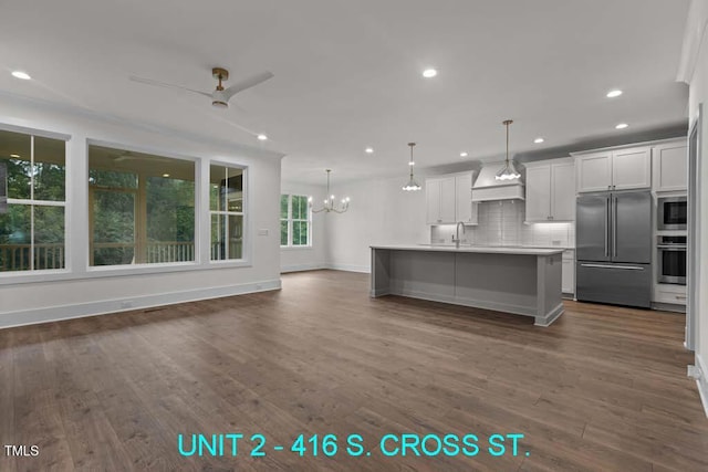 kitchen featuring built in appliances, light countertops, ceiling fan with notable chandelier, decorative backsplash, and dark wood-style floors