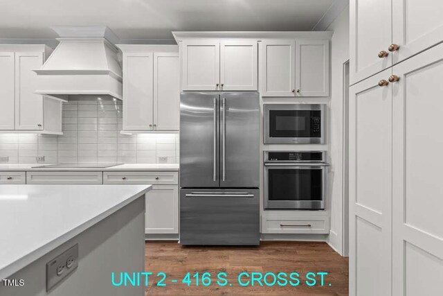 kitchen with light countertops, appliances with stainless steel finishes, custom range hood, and white cabinetry
