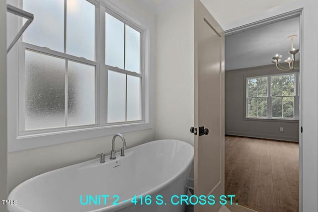 full bath with an inviting chandelier, a soaking tub, and wood finished floors