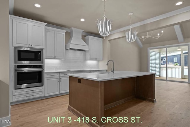 kitchen featuring built in microwave, a sink, custom exhaust hood, a notable chandelier, and stainless steel oven