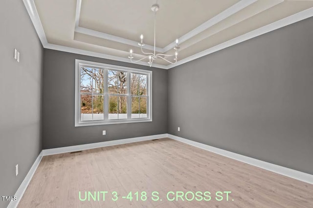 spare room with baseboards, a raised ceiling, wood finished floors, and a notable chandelier