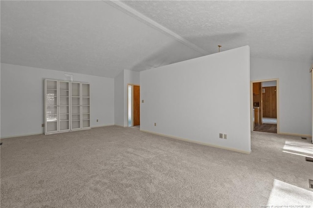 carpeted spare room with vaulted ceiling, a textured ceiling, and baseboards