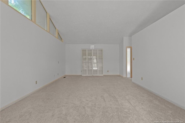 unfurnished room with lofted ceiling, light carpet, and baseboards