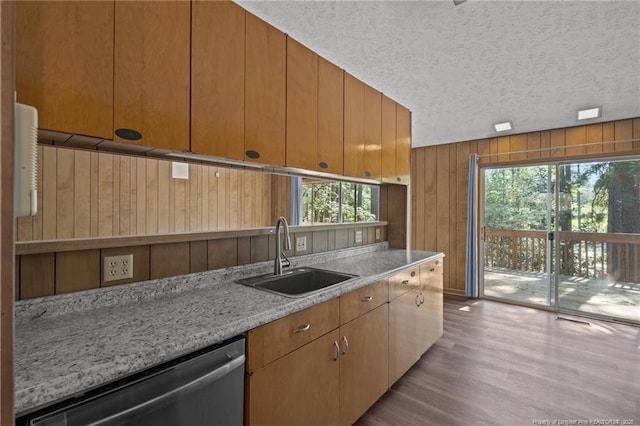 kitchen featuring stainless steel dishwasher, a sink, a textured ceiling, wood finished floors, and wooden walls