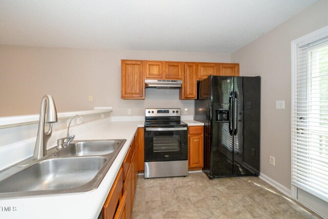 kitchen with brown cabinets, a sink, under cabinet range hood, electric range, and black fridge