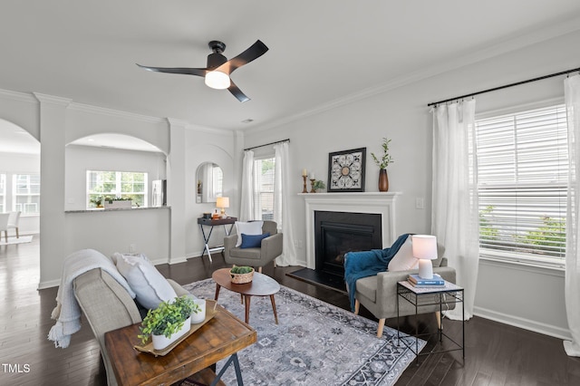 living area featuring baseboards, wood finished floors, plenty of natural light, arched walkways, and crown molding