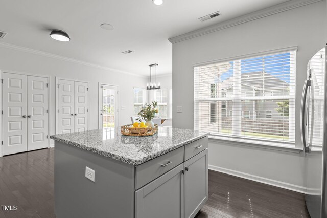 kitchen with crown molding, freestanding refrigerator, a chandelier, dark wood-style floors, and light stone counters