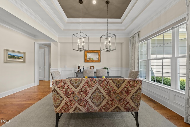 dining space with ornamental molding, a tray ceiling, wood finished floors, and a notable chandelier