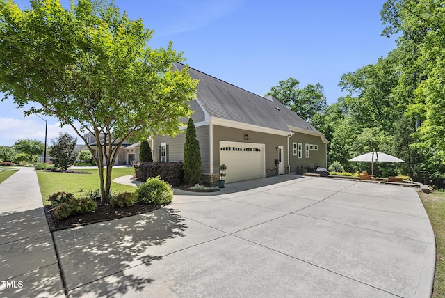 view of side of home with roof with shingles, a garage, a yard, concrete driveway, and stone siding