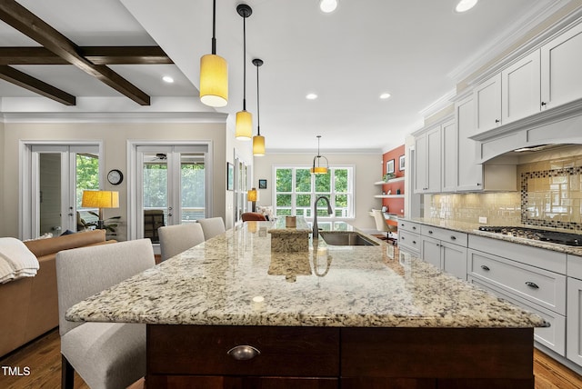 kitchen with a kitchen breakfast bar, crown molding, stainless steel gas cooktop, a large island with sink, and a sink