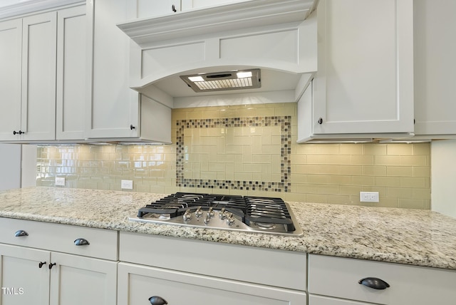 kitchen with light stone counters, stainless steel gas cooktop, premium range hood, white cabinetry, and decorative backsplash