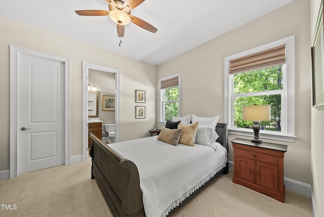 bedroom featuring light colored carpet, baseboards, ensuite bathroom, and ceiling fan