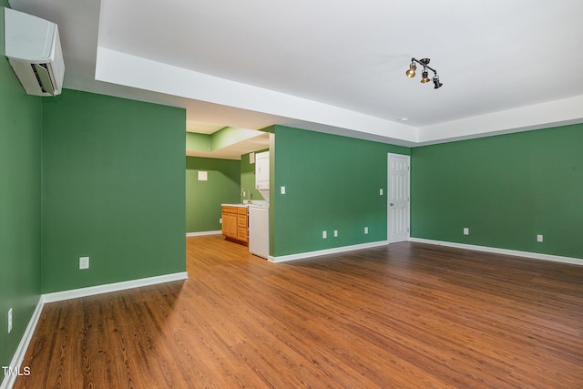 spare room featuring wood finished floors, a raised ceiling, baseboards, and a wall mounted AC