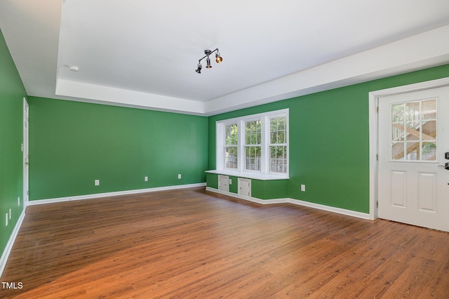 empty room with baseboards, wood finished floors, and a tray ceiling