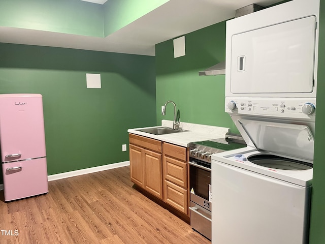 clothes washing area with laundry area, a sink, baseboards, stacked washer / dryer, and light wood-type flooring