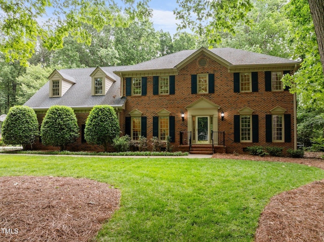 colonial-style house with brick siding, a front lawn, and a shingled roof