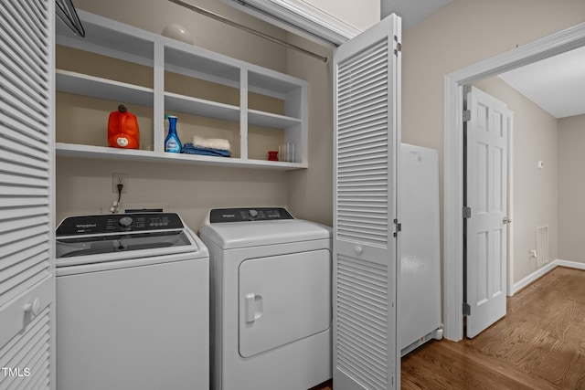 clothes washing area featuring wood finished floors, washing machine and dryer, and baseboards