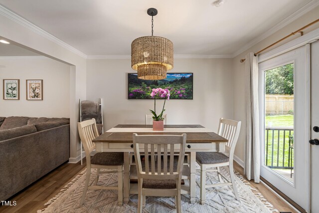 dining room featuring light wood-style flooring, baseboards, a notable chandelier, and crown molding