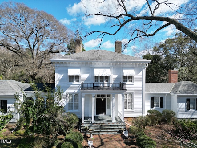 view of front of house with covered porch, a chimney, and a balcony