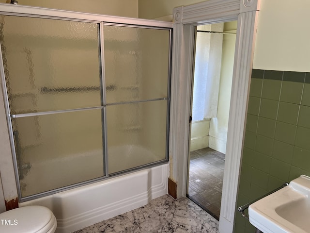 full bath featuring toilet, bath / shower combo with glass door, and tile walls