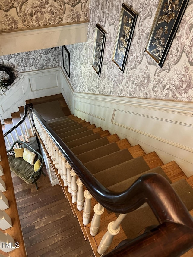 stairs featuring wainscoting, wallpapered walls, and wood-type flooring