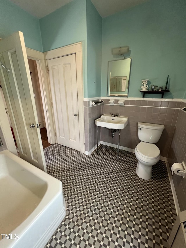 bathroom with tile walls, wainscoting, a sink, and toilet