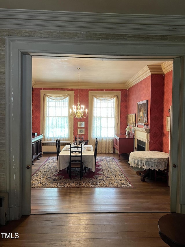 dining area with radiator, a chandelier, wallpapered walls, hardwood / wood-style floors, and ornamental molding
