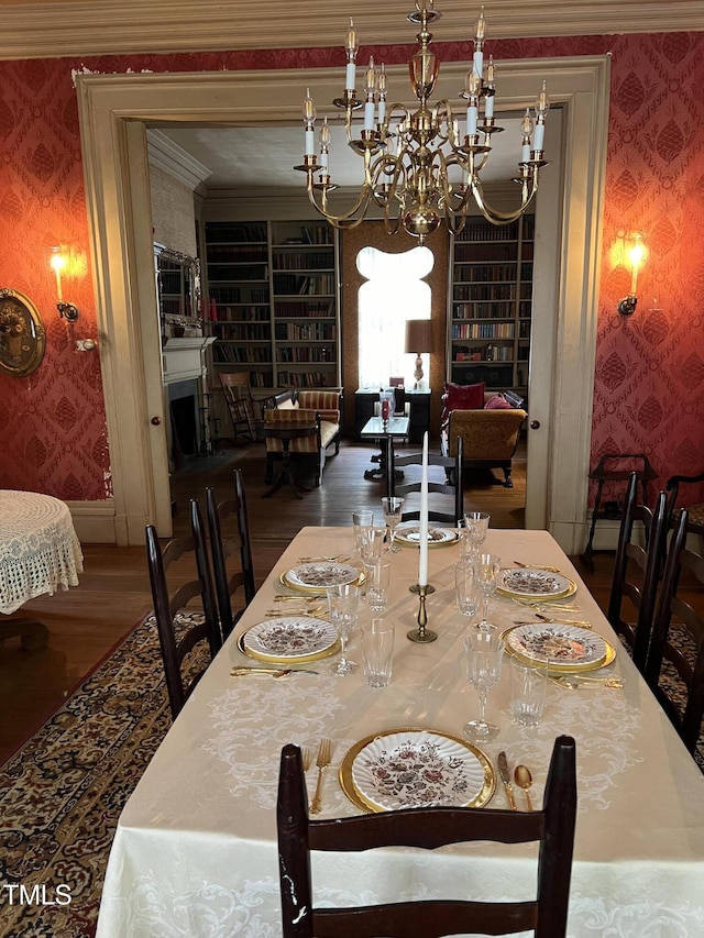 dining area with an inviting chandelier, ornamental molding, wood finished floors, and wallpapered walls