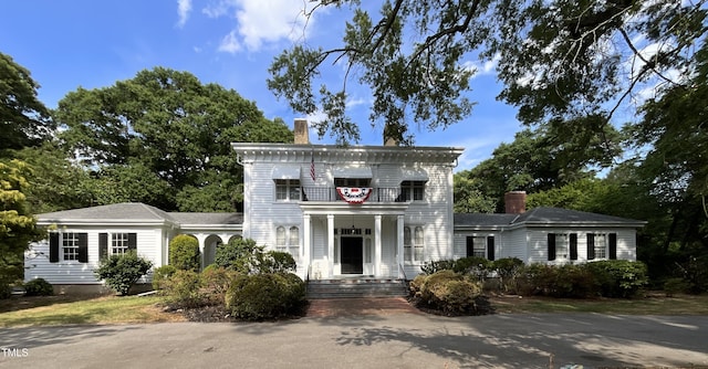 italianate-style house featuring a chimney, a balcony, and covered porch