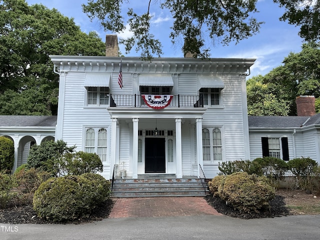italianate home with a chimney, a porch, and a balcony