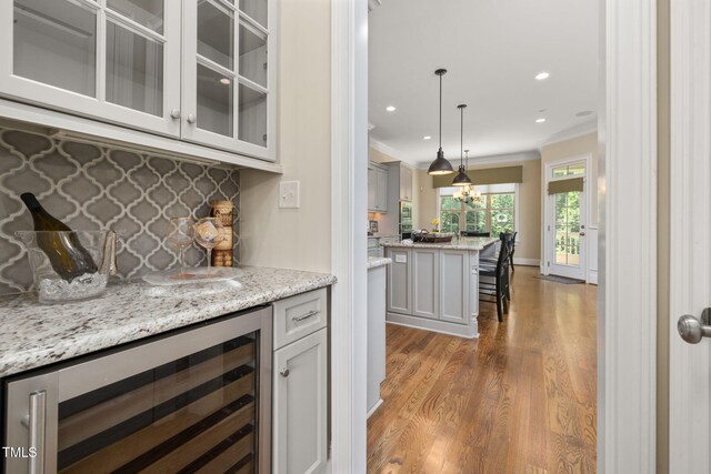 indoor dry bar with wine cooler, ornamental molding, decorative backsplash, wood finished floors, and pendant lighting