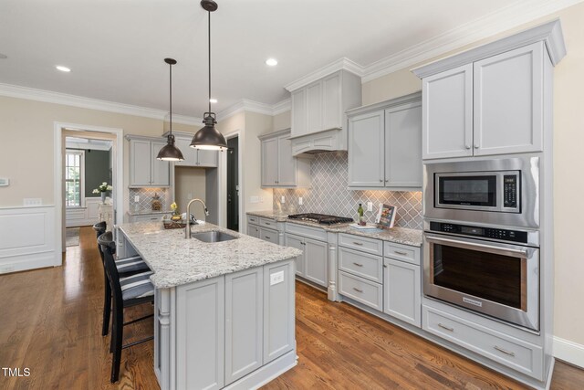 kitchen featuring appliances with stainless steel finishes, a sink, light stone countertops, tasteful backsplash, and dark wood-type flooring