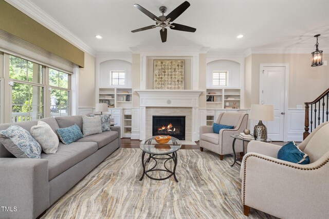 living area featuring a tiled fireplace, ceiling fan, ornamental molding, stairs, and recessed lighting