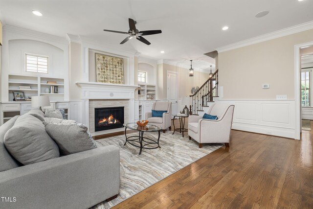 living area featuring crown molding, a tiled fireplace, wood finished floors, ceiling fan, and stairs