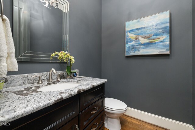 half bath with wood finished floors, baseboards, vanity, and toilet