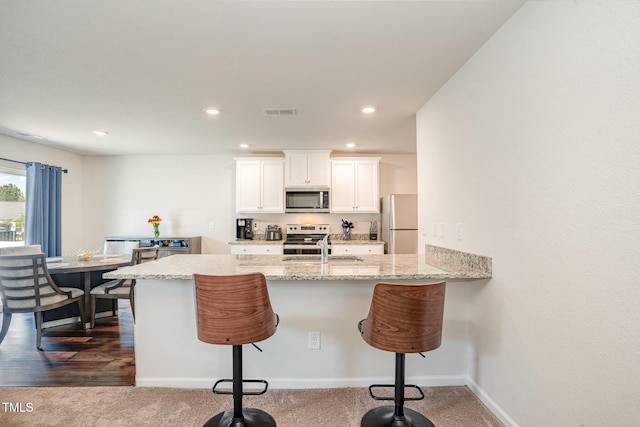 kitchen featuring visible vents, a breakfast bar area, white cabinets, and stainless steel appliances