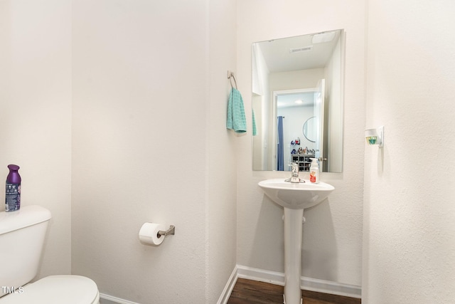 bathroom with baseboards, toilet, wood finished floors, and visible vents