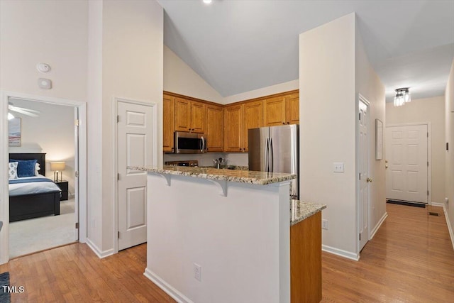 kitchen with vaulted ceiling, light stone countertops, stainless steel appliances, and light wood-style flooring