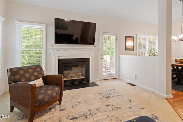 carpeted living room featuring an inviting chandelier, a fireplace with flush hearth, baseboards, and visible vents