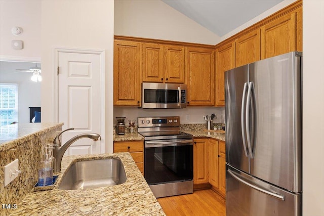 kitchen with brown cabinets, stainless steel appliances, vaulted ceiling, and a sink